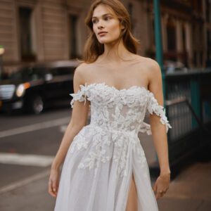 Netta BenShabu Sylvie Wedding Dress - A-line tulle gown featuring floral applique throughout the bodice with off the shoulder straps and front slit skirt.