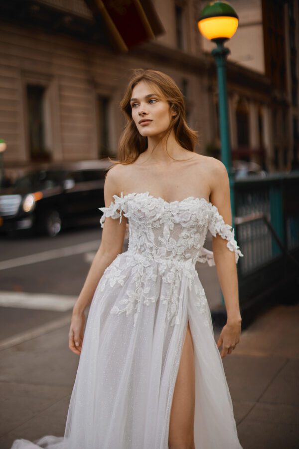 Netta BenShabu Sylvie Wedding Dress - A-line tulle gown featuring floral applique throughout the bodice with off the shoulder straps and front slit skirt.