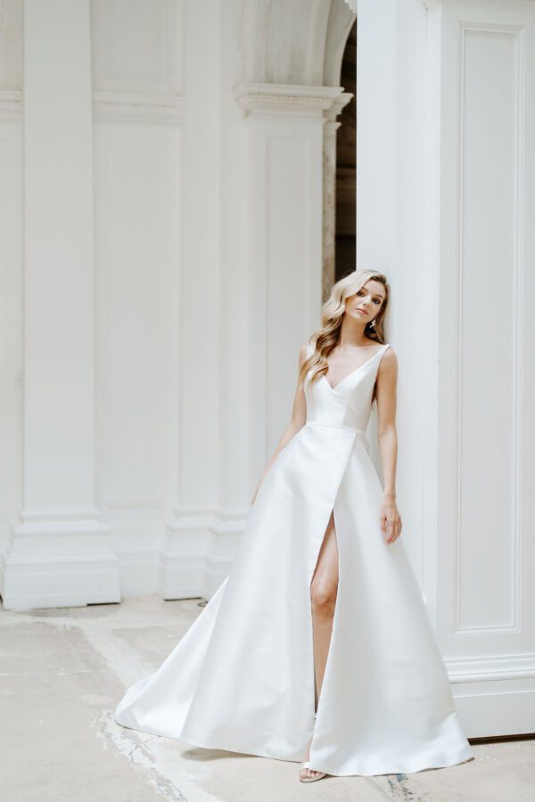 Suzanne Neville Coworth Wedding Dress - A Line with structured bodice, plunging low neckline and back, straps, full skirt with slit in a Duchess satin mikado fabric.