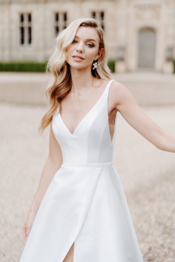 Suzanne Neville Coworth Wedding Dress - A Line with structured bodice, plunging low neckline and back, straps, full skirt with slit in a Duchess satin mikado fabric.