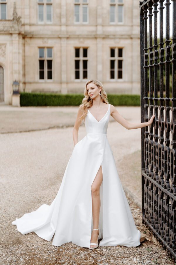 Suzanne Neville Coworth Wedding Dress - A Line with structured bodice, plunging low neckline and back, straps, full skirt with slit in a Duchess satin mikado fabric.