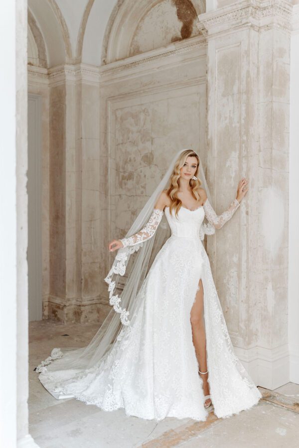 Suzanne Neville Wellesley Wedding Dress - Modifies A Line dress with a sweetheart neckline, illusion lace off the shoulder detachable sleeves, open slit on front and fitted corset bodice. 