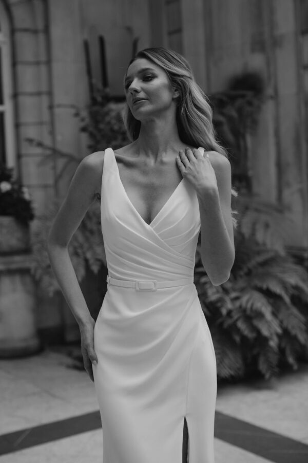 Suzanne Neville Sibelious Wedding Dress - Modified A Line style dress with V -Neckline, draped fitted bodice, front slit on skirt and belt detail.