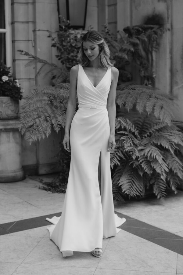 Suzanne Neville Sibelious Wedding Dress - Modified A Line style dress with V -Neckline, draped fitted bodice, front slit on skirt and belt detail.