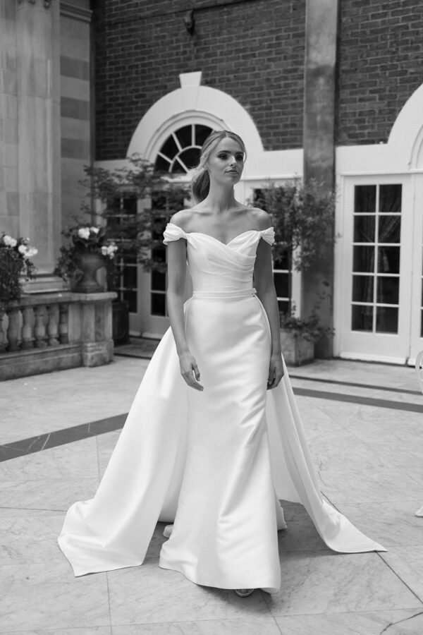 Suzanne Neville Marquez Wedding Dress - Fit and flare style dress with ruched bodice, sweetheart neckline, Off the shoulder sleeves, low V-Back + overskirt.