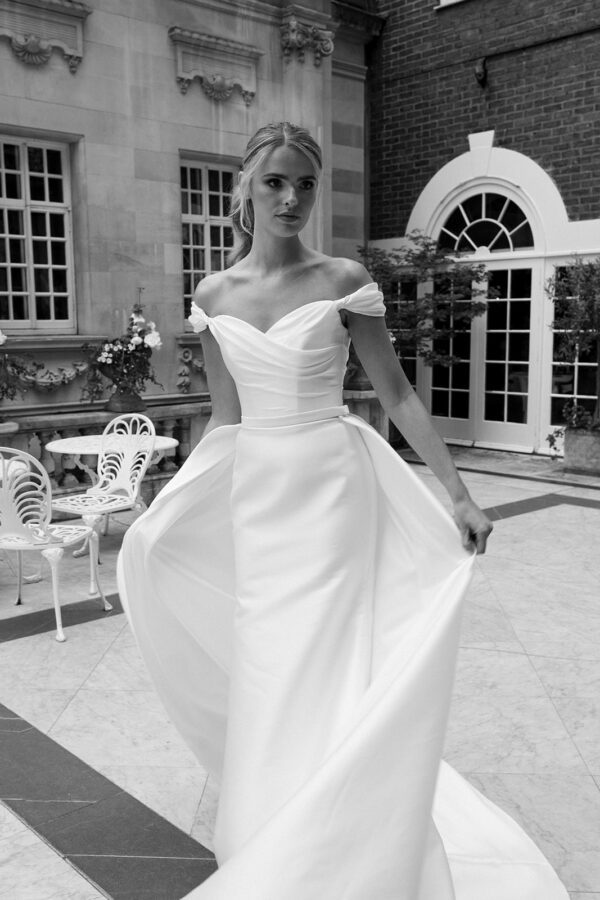 Suzanne Neville Marquez Wedding Dress - Fit and flare style dress with ruched bodice, sweetheart neckline, Off the shoulder sleeves, low V-Back + overskirt.