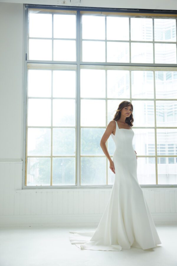 Suzanne Neville Peninsula Wedding Dress - An elegant fit-and-flare gown featuring a modern square neckline, a structured corset bodice, delicate thin straps, and a U-shaped back adorned with covered buttons for a timeless, refined finish.