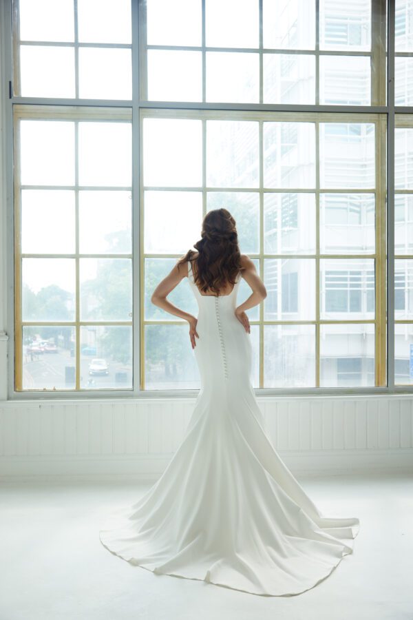 Suzanne Neville Peninsula Wedding Dress - An elegant fit-and-flare gown featuring a modern square neckline, a structured corset bodice, delicate thin straps, and a U-shaped back adorned with covered buttons for a timeless, refined finish.