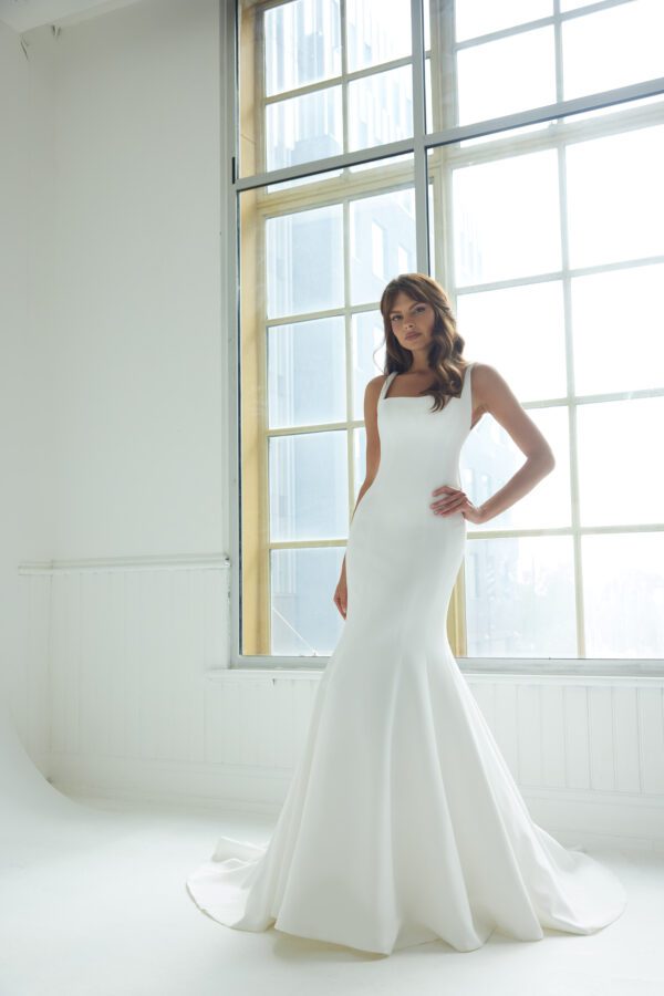 Suzanne Neville Peninsula Wedding Dress - An elegant fit-and-flare gown featuring a modern square neckline, a structured corset bodice, delicate thin straps, and a U-shaped back adorned with covered buttons for a timeless, refined finish.