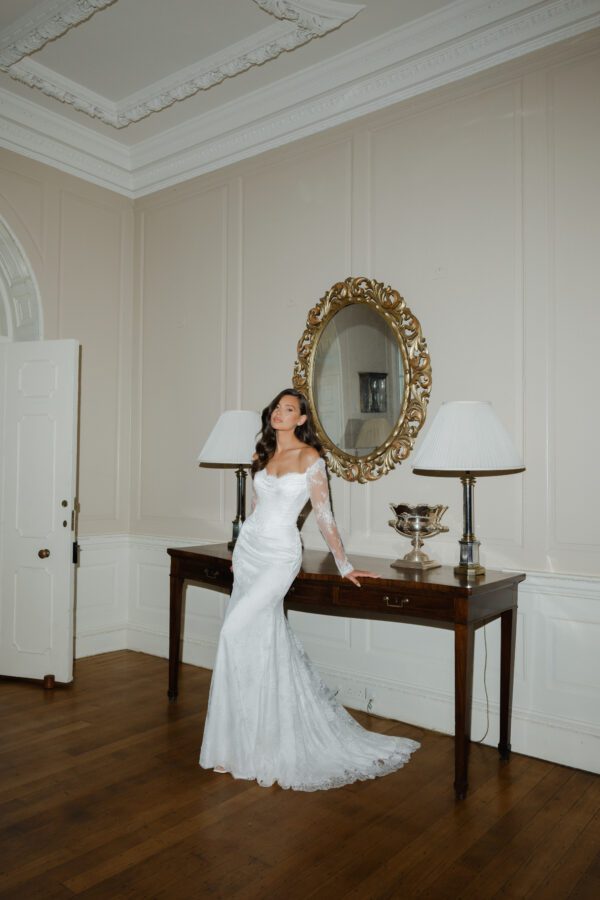 Suzanne Neville Camomile Wedding Dress - Fit and Flare style dress with beautiful bateau neckline, all over lace, off the shoulder long sleeves, V cut on waist, V-back and covered buttons. 