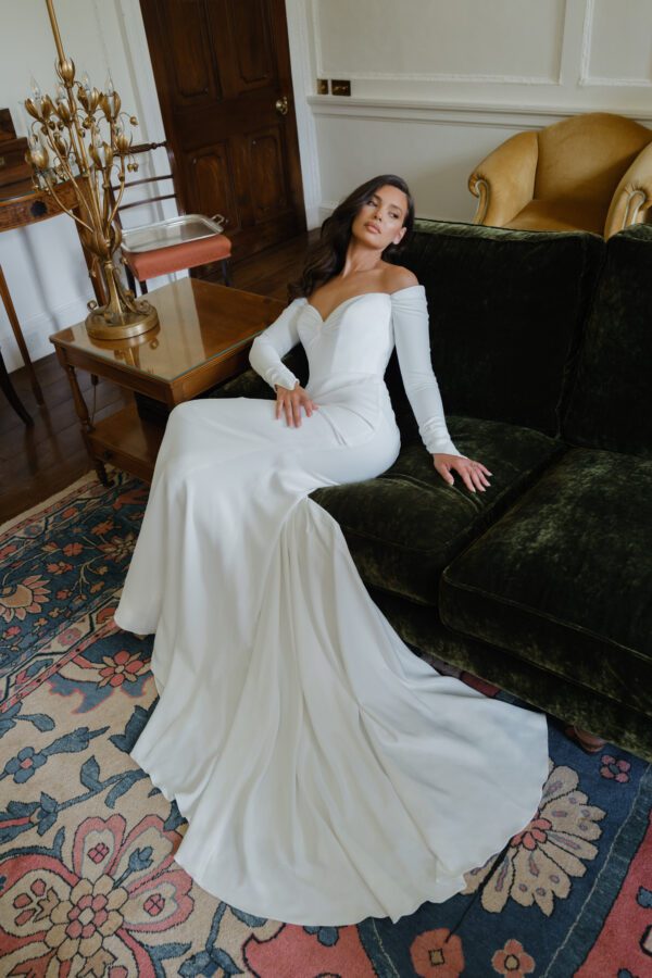 Suzanne Neville Dehlia Wedding Dress - Fit and flare style dress with a beautiful minimal and timeless look, featuring off the shoulder long sleeves, sweetheart neckline, low V-back, ruched detail in back. 