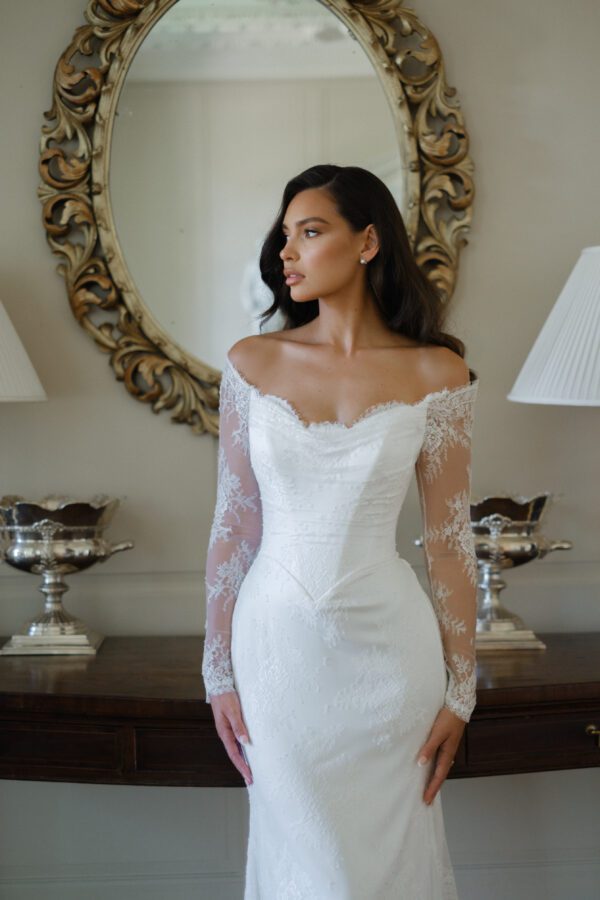 Suzanne Neville Camomile Wedding Dress - Fit and Flare style dress with beautiful bateau neckline, all over lace, off the shoulder long sleeves, V cut on waist, V-back and covered buttons. 