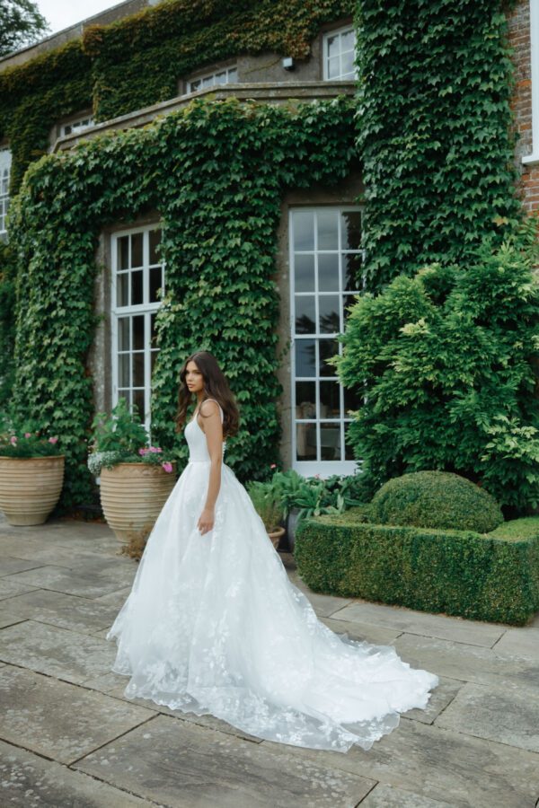 Suzanne Neville Moonlight Wedding Dress - A Line style dress with a squared neckline, corset bodice, flowy skirt with side slit and thin belt detail.