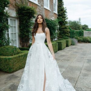 Suzanne Neville Moonlight Wedding Dress - A Line style dress with a squared neckline, corset bodice, flowy skirt with side slit and thin belt detail.