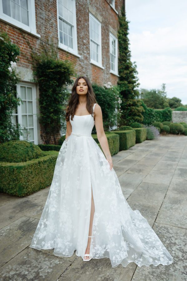 Suzanne Neville Moonlight Wedding Dress - A Line style dress with a squared neckline, corset bodice, flowy skirt with side slit and thin belt detail.