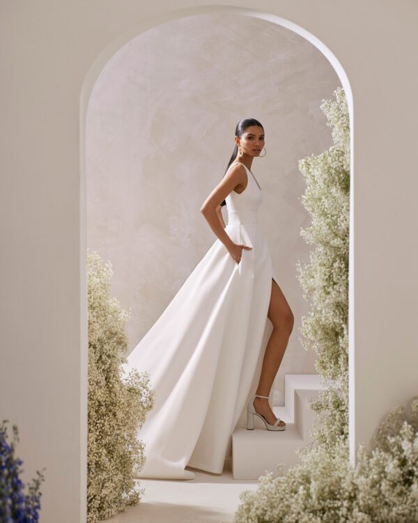 Rosa Clará Taori Wedding Dress - Elegant princess wedding dress crafted in cloqué. Featuring a V-neckline, V-back and straps. The pockets at the skirt, front slit and sash complete the look.