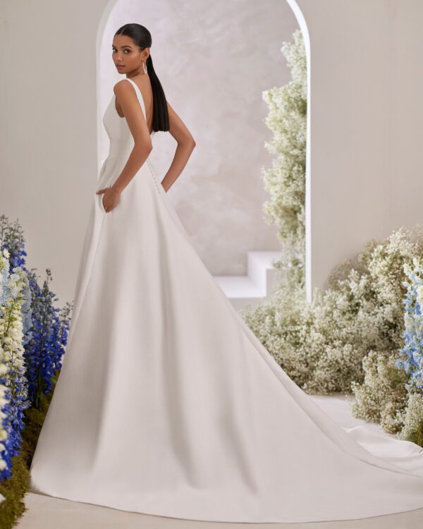 Rosa Clará Taori Wedding Dress - Elegant princess wedding dress crafted in cloqué. Featuring a V-neckline, V-back and straps. The pockets at the skirt, front slit and sash complete the look.