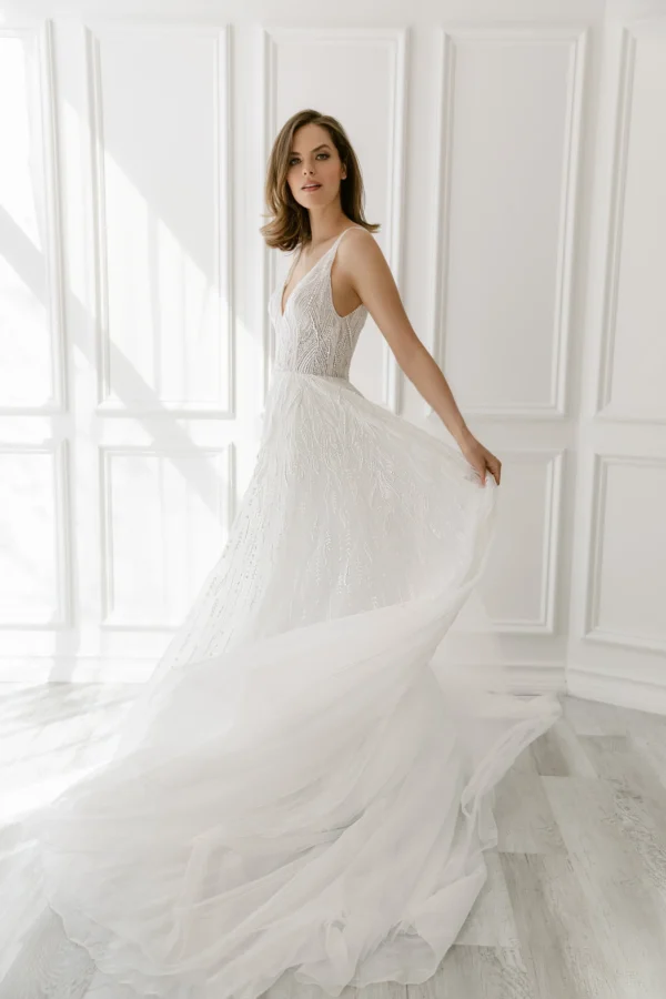 Enaura Margo Wedding Dress - A Line style dress adorned in pearls and glittering beads features a V-neck, V-back, and flowy tulle skirt.