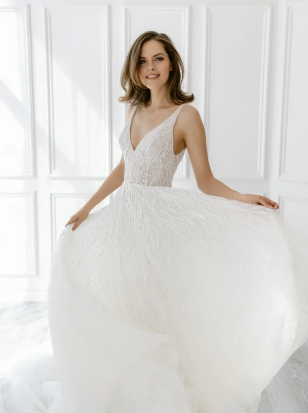 Enaura Margo Wedding Dress - A Line style dress adorned in pearls and glittering beads features a V-neck, V-back, and flowy tulle skirt.